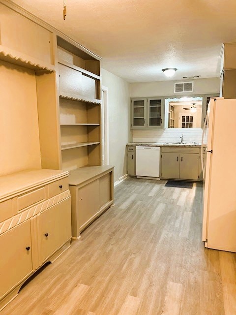 kitchen with light wood finished floors, light countertops, visible vents, glass insert cabinets, and white appliances