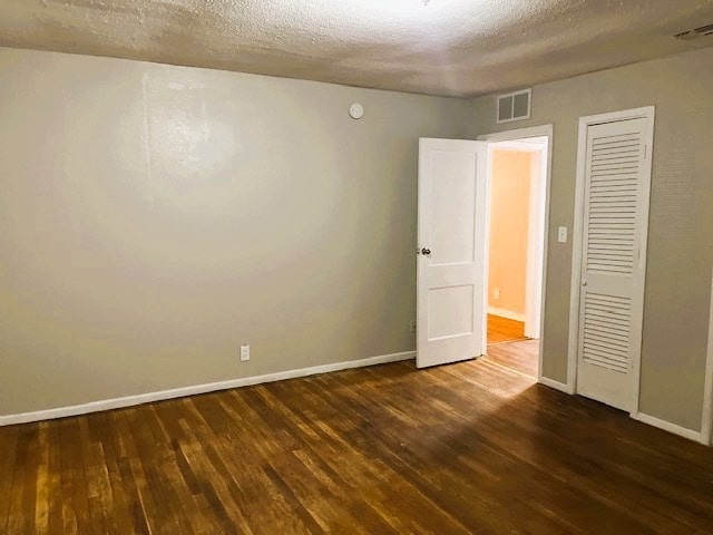 unfurnished bedroom featuring a textured ceiling, dark wood finished floors, visible vents, and baseboards