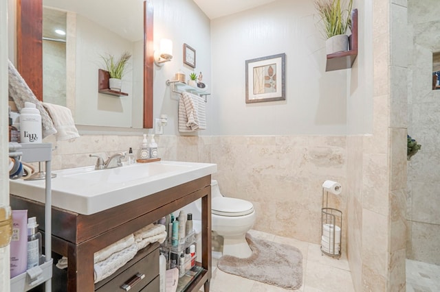 bathroom with tile patterned flooring, vanity, toilet, a wainscoted wall, and tile walls