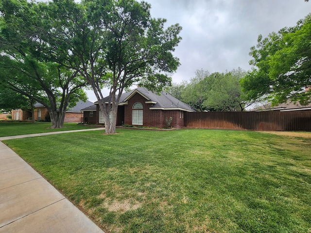 ranch-style house featuring brick siding, fence, and a front yard