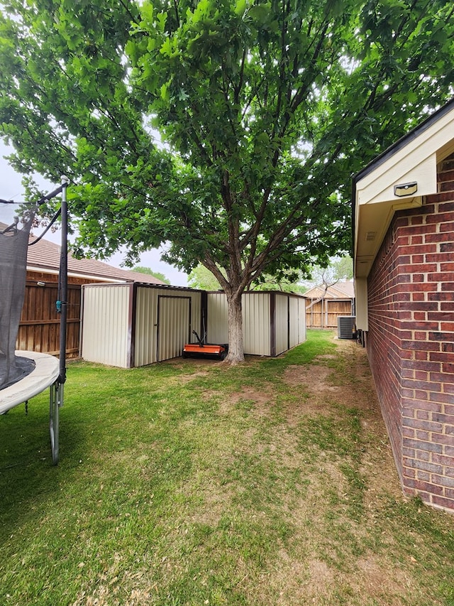 view of yard with fence, an outdoor structure, a trampoline, and a storage unit
