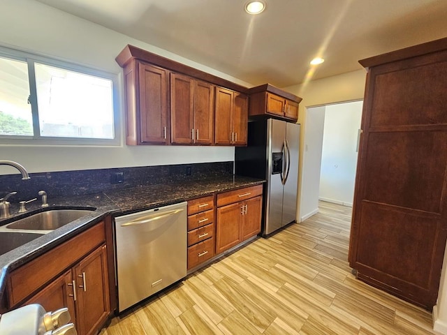 kitchen featuring light hardwood / wood-style floors, dark stone countertops, sink, and appliances with stainless steel finishes