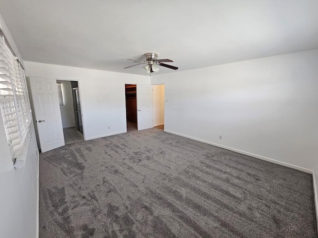 unfurnished bedroom featuring dark colored carpet, ceiling fan, a walk in closet, and a closet