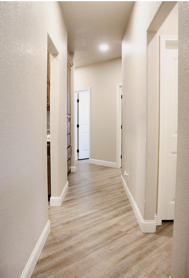 hall featuring light wood-type flooring, baseboards, and a textured wall