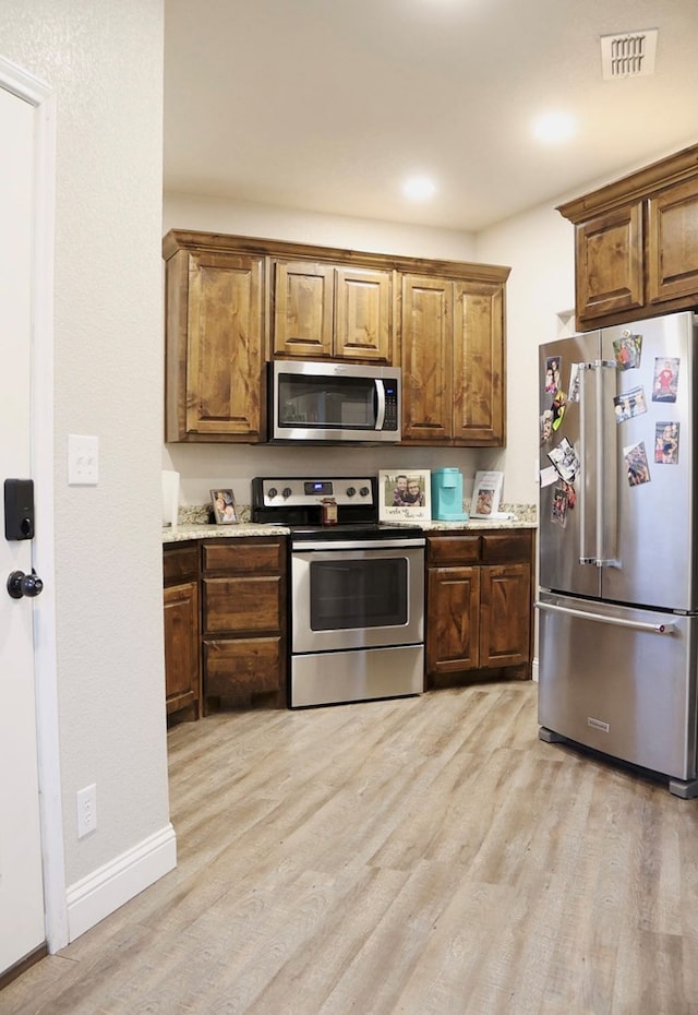 kitchen featuring visible vents, appliances with stainless steel finishes, brown cabinetry, light wood-style floors, and baseboards