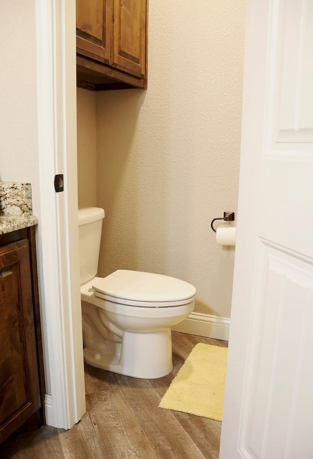 half bathroom featuring toilet, baseboards, wood finished floors, and vanity