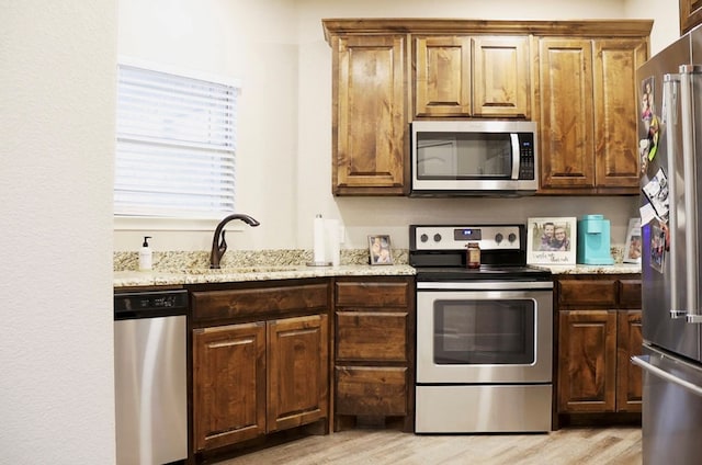 kitchen featuring light wood-type flooring, light stone countertops, stainless steel appliances, and a sink