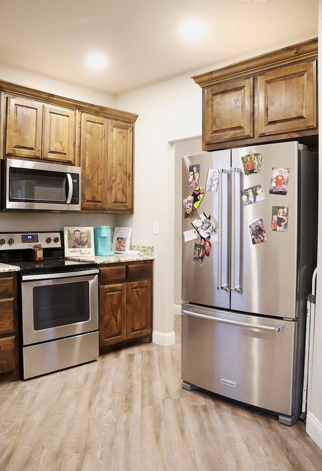 kitchen with baseboards, brown cabinetry, light wood-style flooring, light stone countertops, and stainless steel appliances