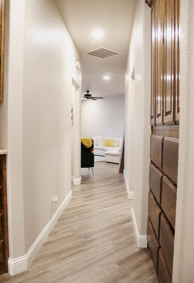 hallway with a textured wall, light wood finished floors, visible vents, and baseboards