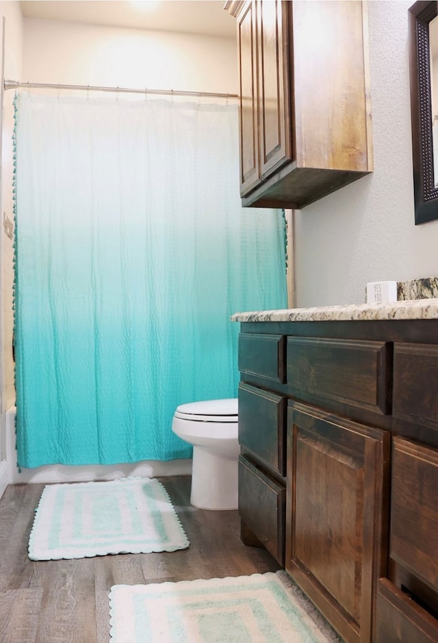 bathroom featuring toilet, shower / bath combination with curtain, wood finished floors, and vanity