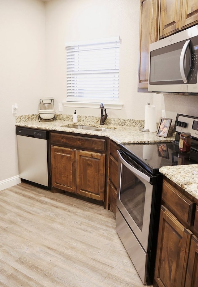 kitchen featuring light wood finished floors, appliances with stainless steel finishes, a sink, and light stone counters