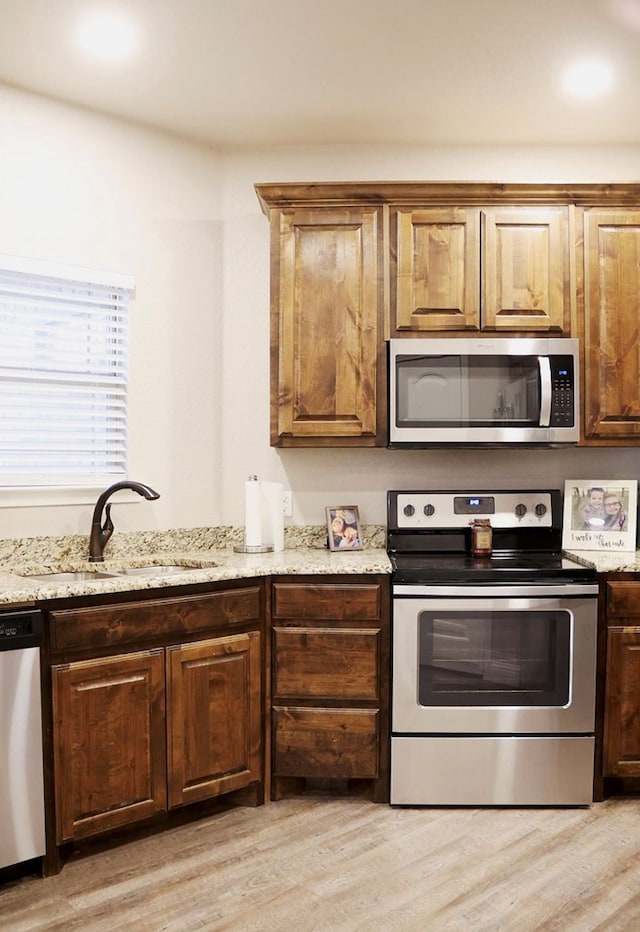 kitchen featuring appliances with stainless steel finishes, a sink, light stone counters, and light wood-style floors