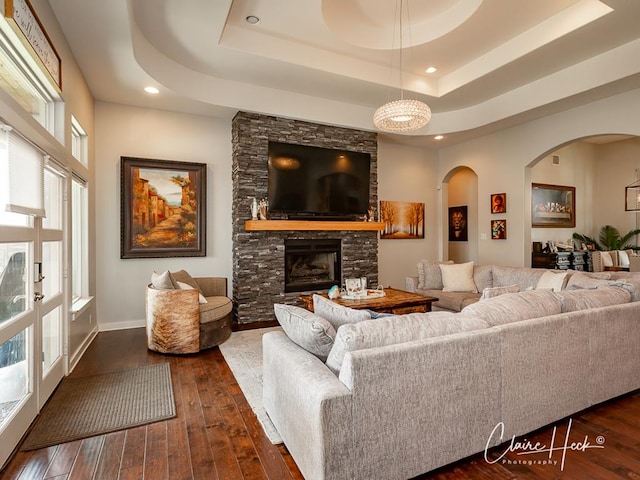5300 Balfour Ct, Midland, TX 79707 - living room with arched walkways, dark wood-type flooring, a tray ceiling, a stone fireplace, and recessed lighting
