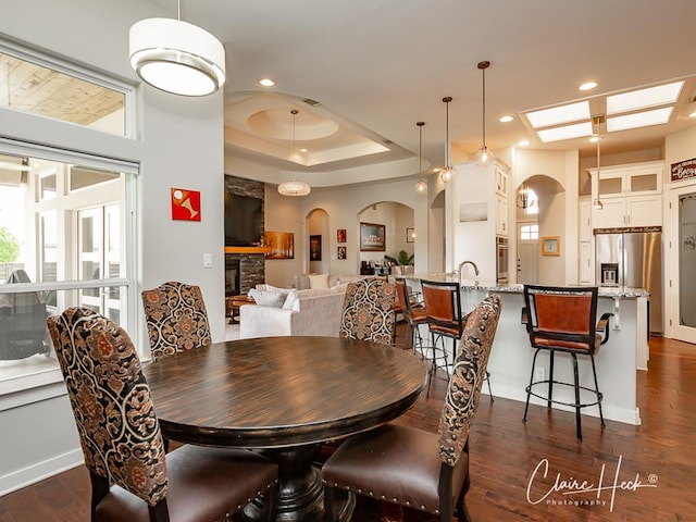 5300 Balfour Ct, Midland, TX 79707 - dining area featuring dark wood-style flooring, a fireplace, arched walkways, recessed lighting, and a raised ceiling