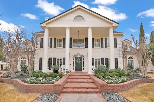 neoclassical home featuring a porch and brick siding