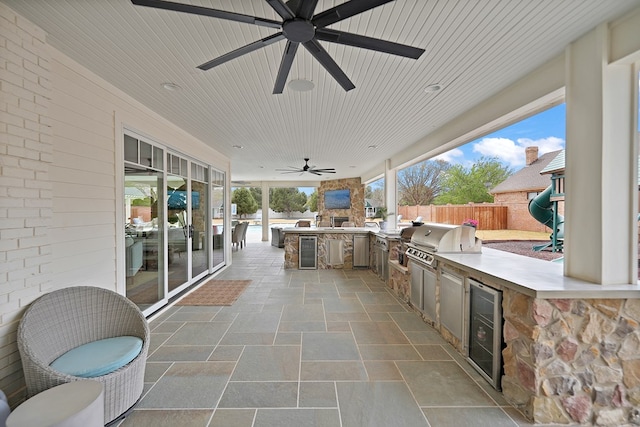view of patio with fence, area for grilling, a ceiling fan, beverage cooler, and an outdoor kitchen