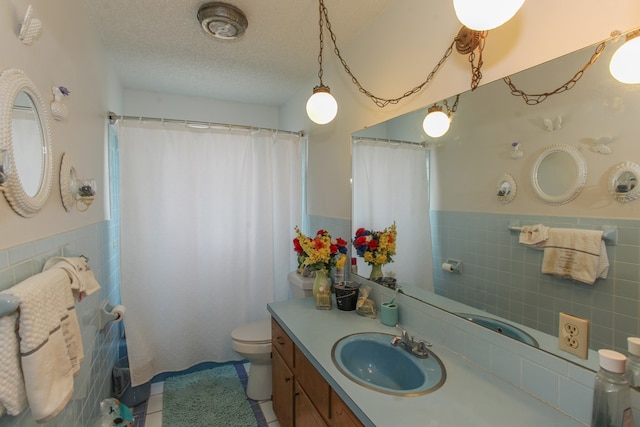 bathroom featuring tile patterned flooring, a textured ceiling, toilet, vanity, and tile walls