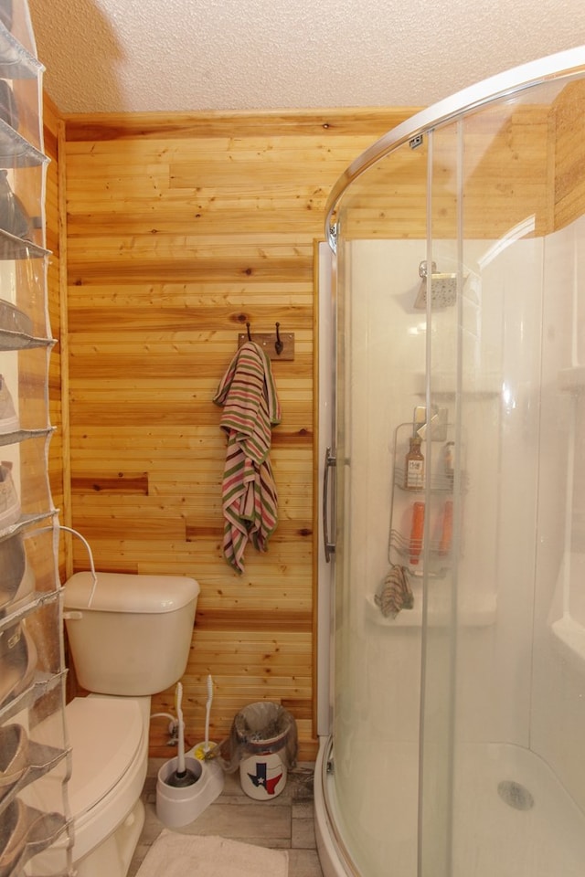 bathroom featuring a textured ceiling, toilet, a shower with door, and wood walls