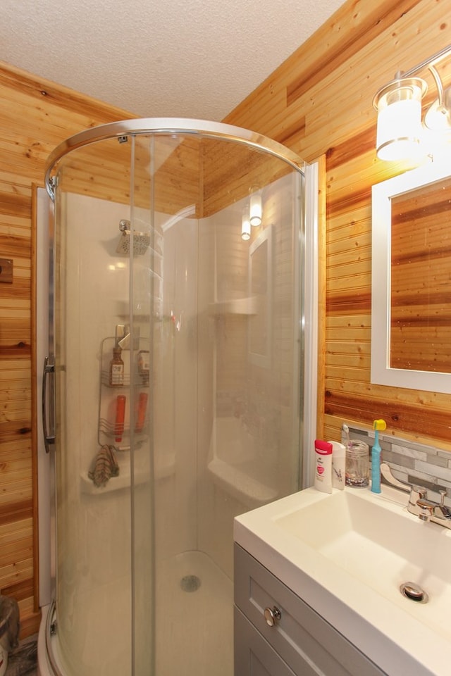 bathroom with vanity, backsplash, wooden walls, walk in shower, and a textured ceiling