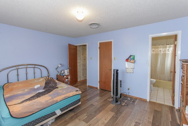 bedroom with a textured ceiling, dark wood-type flooring, and connected bathroom