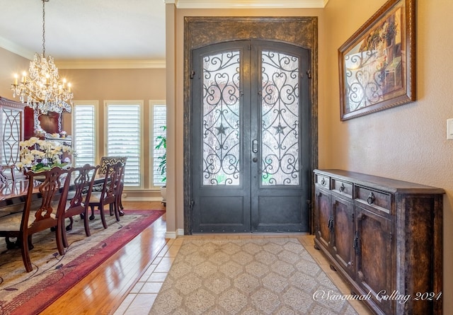 foyer with crown molding, french doors, light hardwood / wood-style flooring, and an inviting chandelier