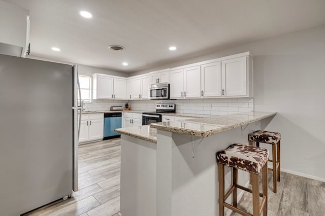 4003 Angelina Dr, Midland, TX 79705 - kitchen with stainless steel appliances, a peninsula, light wood-style floors, decorative backsplash, and a kitchen breakfast bar