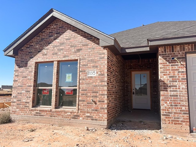 doorway to property with brick siding and a shingled roof