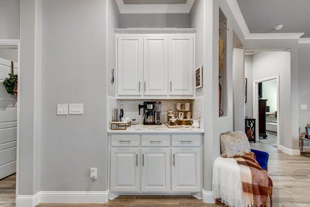 bar with light wood finished floors, baseboards, tasteful backsplash, and ornamental molding