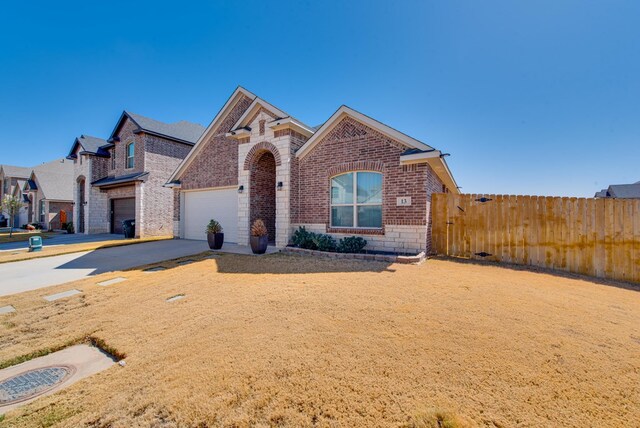 view of front of home featuring stone siding, fence, a garage, concrete driveway, and brick siding