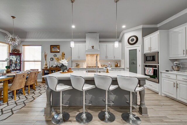 13 La Cresta Ave, Odessa, TX 79765 - kitchen featuring appliances with stainless steel finishes, light countertops, a kitchen bar, light wood finished floors, and ornamental molding