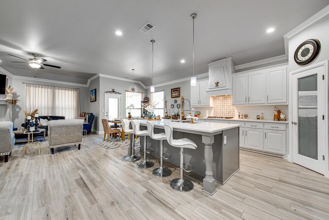 kitchen with light countertops, a breakfast bar area, open floor plan, custom exhaust hood, and ornamental molding