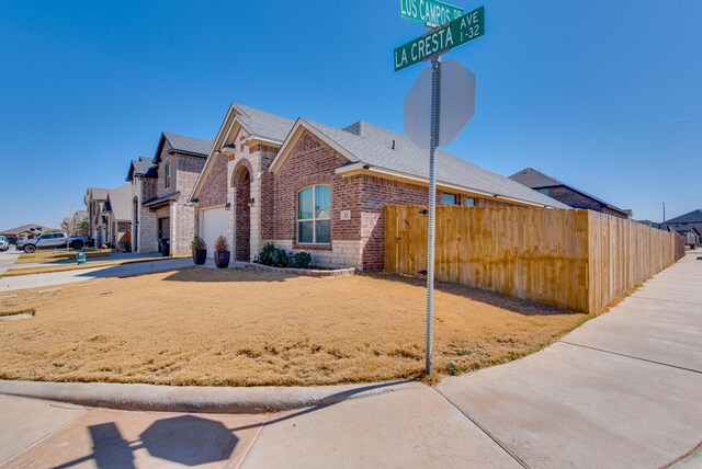 view of property exterior featuring brick siding, driveway, and fence