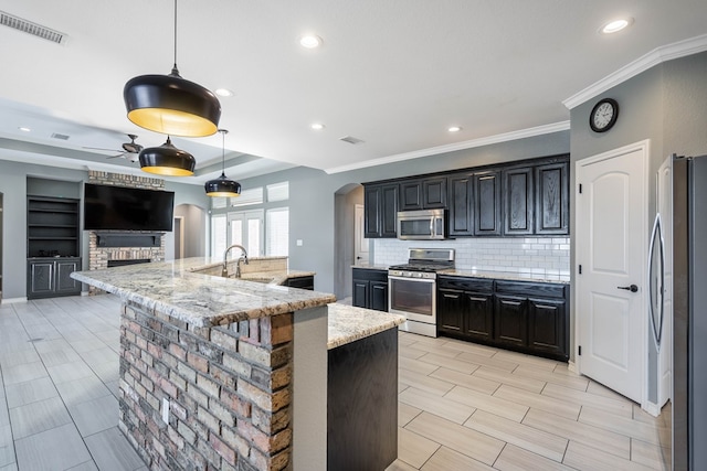 kitchen with appliances with stainless steel finishes, a center island with sink, light stone countertops, pendant lighting, and sink