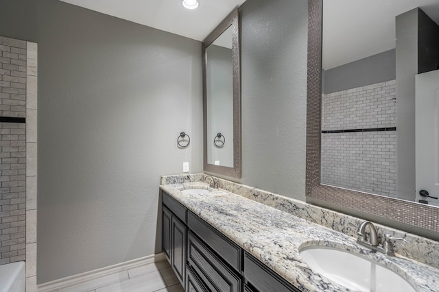 bathroom with double vanity, a bathtub, a textured wall, and baseboards