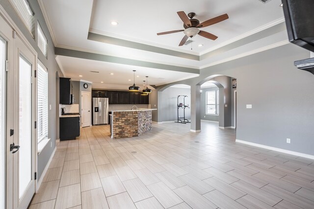 unfurnished living room featuring crown molding, ceiling fan, and a raised ceiling