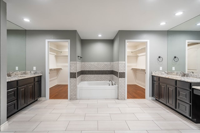 bathroom with a garden tub, two vanities, baseboards, and recessed lighting