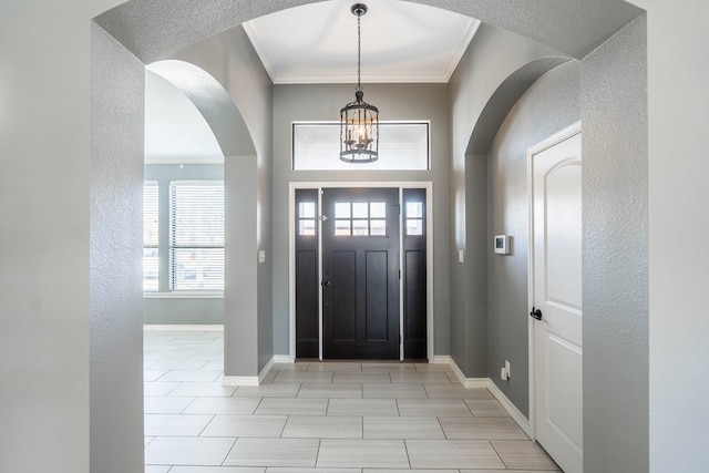 foyer featuring arched walkways, ornamental molding, a chandelier, a textured wall, and baseboards