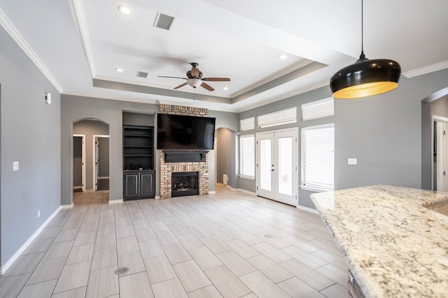 unfurnished living room with a tray ceiling, ornamental molding, a brick fireplace, and ceiling fan