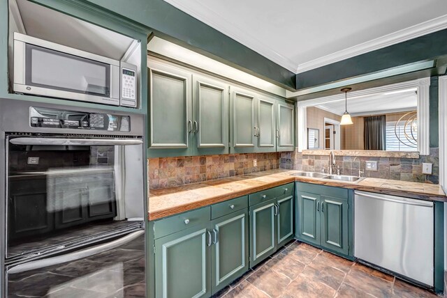 kitchen with sink, green cabinetry, ornamental molding, appliances with stainless steel finishes, and decorative light fixtures