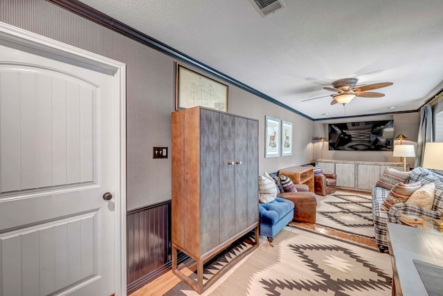 bedroom with ceiling fan, crown molding, light hardwood / wood-style floors, and a textured ceiling