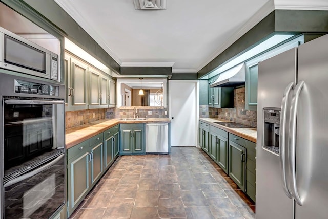 kitchen with decorative backsplash, wall chimney range hood, sink, black appliances, and hanging light fixtures