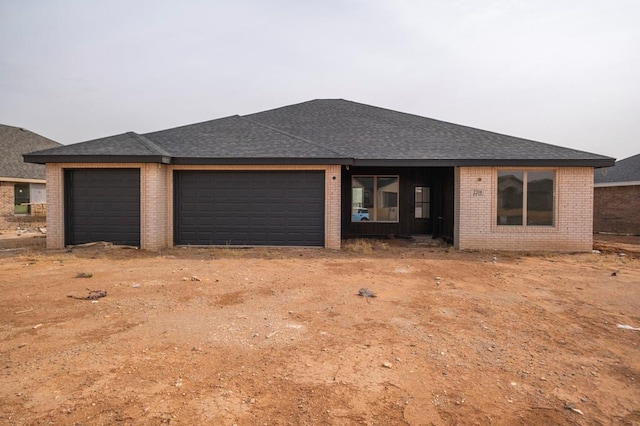 view of front facade featuring a garage, brick siding, driveway, and a shingled roof