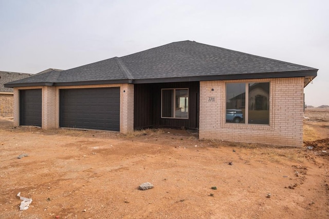 ranch-style house featuring an attached garage, brick siding, and roof with shingles