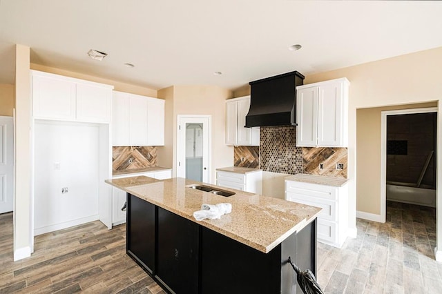 2201 S County Rd 1059, Midland, TX 79706 - kitchen featuring light stone countertops, a center island with sink, light wood-style flooring, custom exhaust hood, and white cabinets
