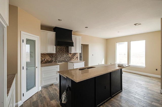 2201 S County Rd 1059, Midland, TX 79706 - kitchen featuring wood finished floors, a center island with sink, custom range hood, white cabinetry, and tasteful backsplash