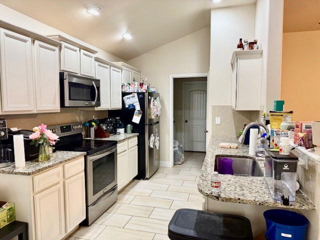 6712 Spur Dr, Midland, TX 79705 - kitchen with appliances with stainless steel finishes, decorative backsplash, lofted ceiling, and light stone counters
