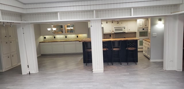 kitchen with sink, white appliances, light hardwood / wood-style flooring, backsplash, and wood counters