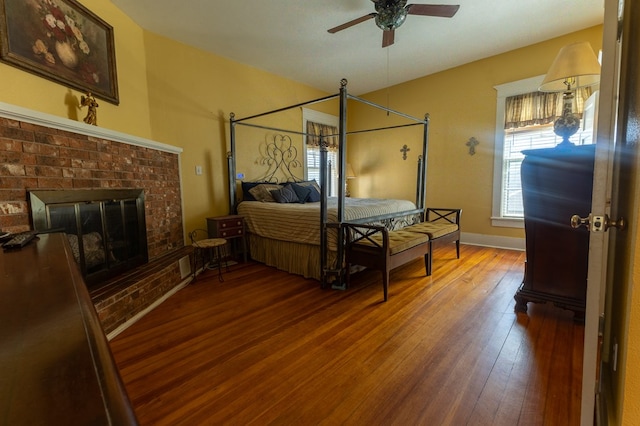 bedroom featuring hardwood / wood-style floors, a brick fireplace, and ceiling fan