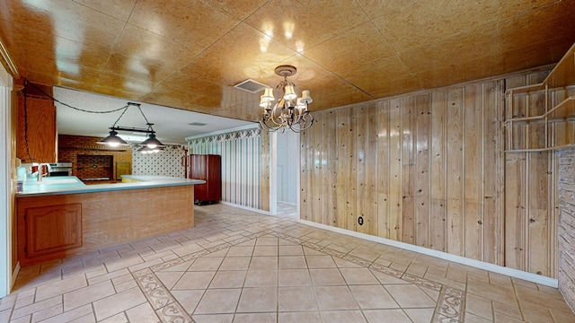 kitchen featuring sink, hanging light fixtures, kitchen peninsula, a chandelier, and wooden walls