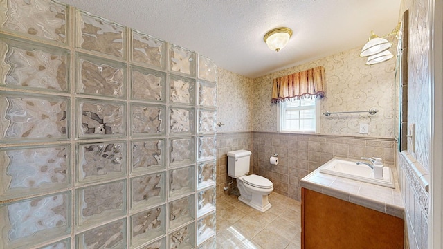 bathroom with tile patterned floors, a textured ceiling, toilet, vanity, and tile walls